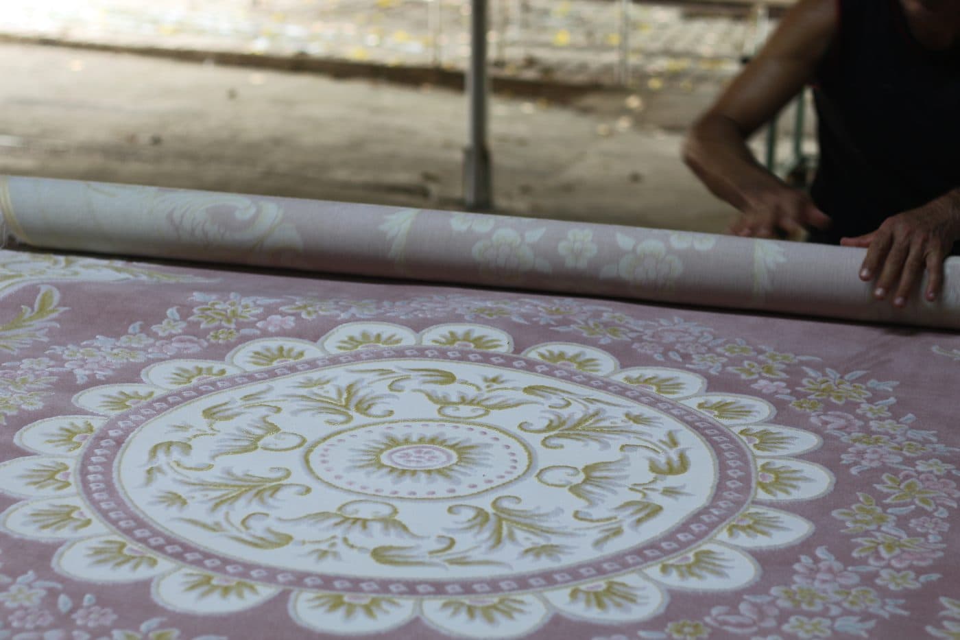 Çalışanlar temizlenen madalyon desenli pembe halıyı rulo hâlinde sarıyor